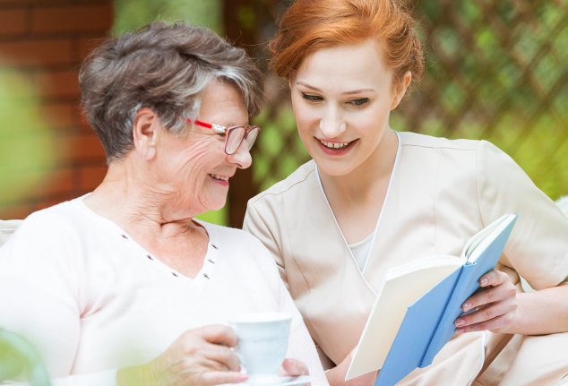 aide and elderly patient smiling while reading a diary